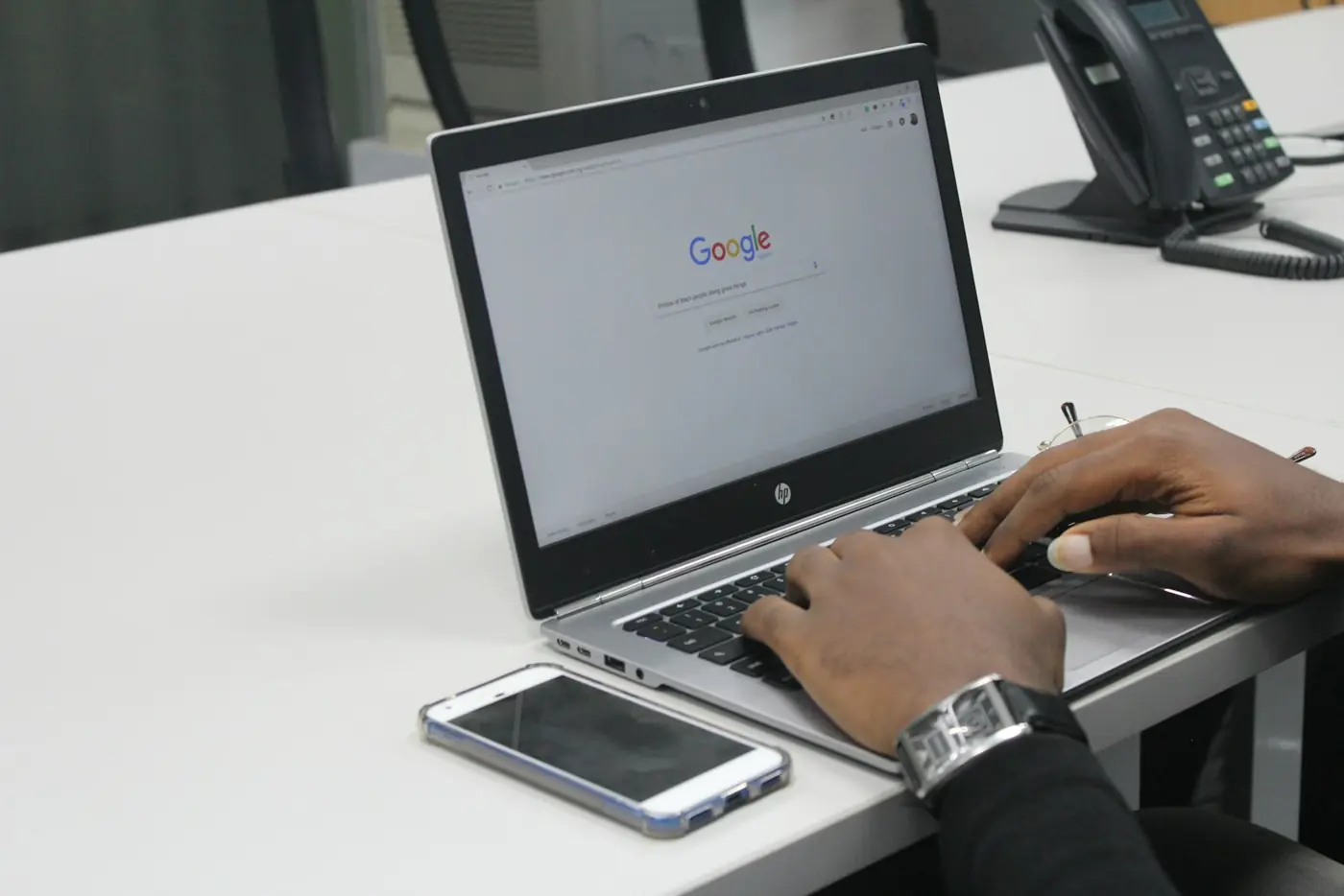 Hands typing a search on a laptop beside a phone