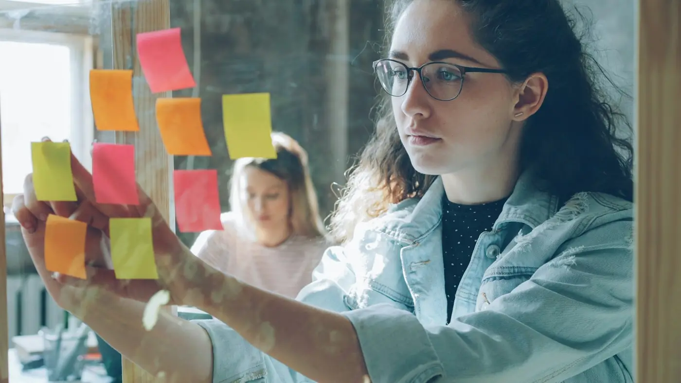 A designer arranging sticky notes on a glass wall while planning a page