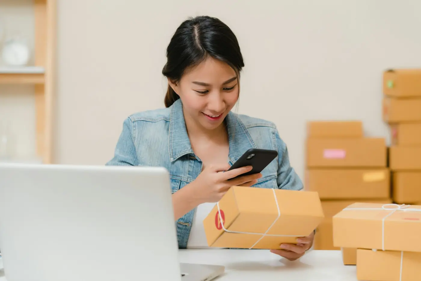 A small business owner checking an order on her phone beside packed parcels