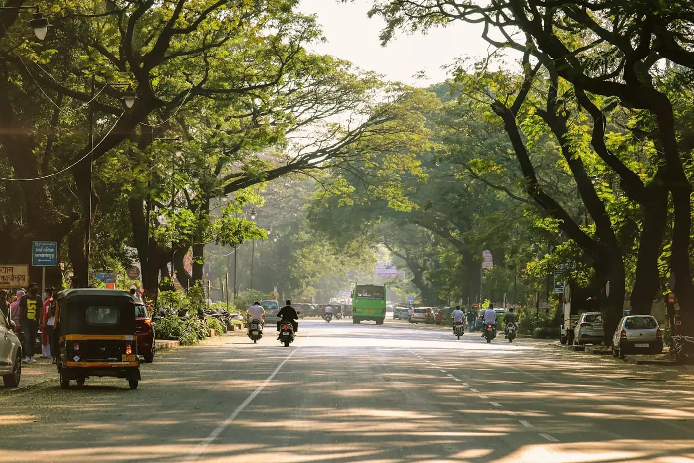 A tree-lined road in Pune with auto rickshaws and scooters