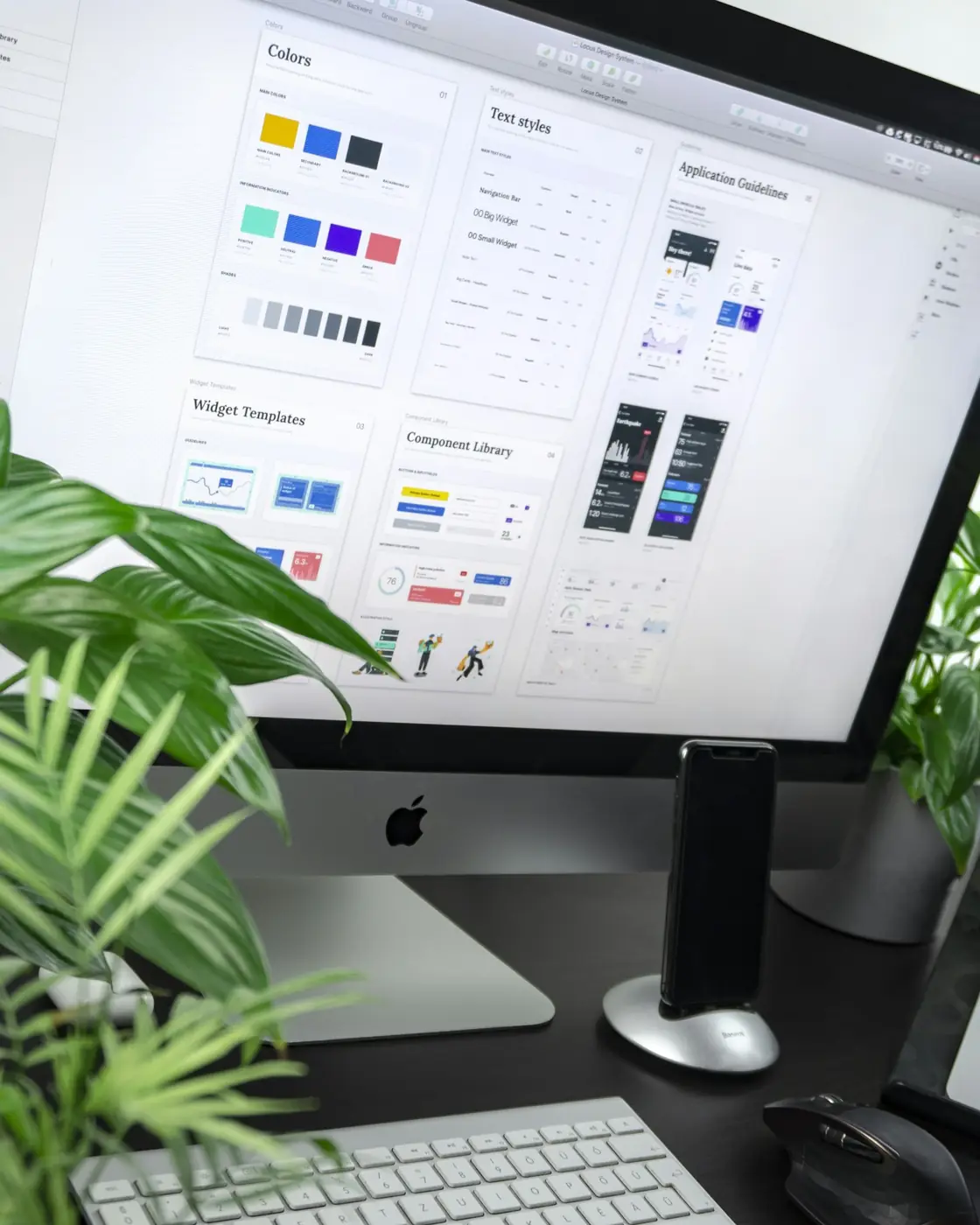 A website design system on a desktop monitor with plants on the desk